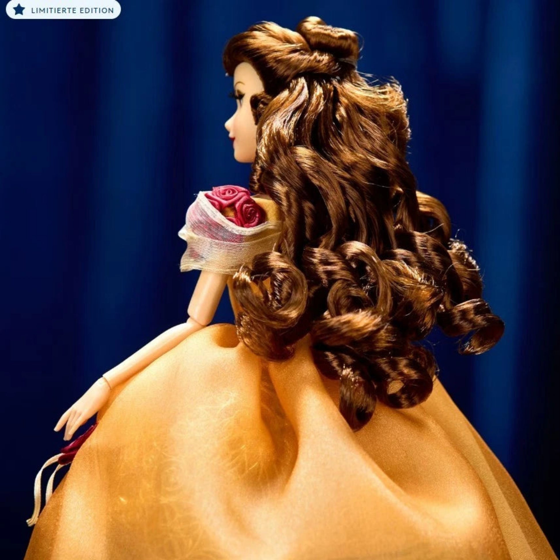 Disney Designer Collection Belle Puppe – Rückansicht der limitierten Edition aus Die Schöne und das Biest mit goldener Robe und detailreicher Lockenfrisur, Nahaufnahme vor blauem Hintergrund