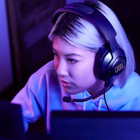 Person mit JBL Quantum Gaming-Headset beim Spielen am PC in violett-blauer Beleuchtung – perfekte Darstellung für immersives Sounderlebnis und moderne Gaming-Ästhetik.