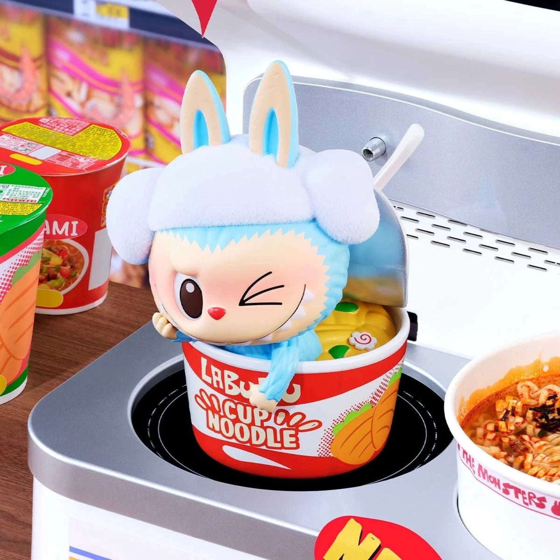 POP MART LABUBU Wacky Mart Figur – verspieltes Art Toy mit blau-weißer Mütze, das auf einer Cup-Noodle-Packung sitzt. Teil der beliebten THE MONSTERS Serie von POP MART im typischen Mini-Supermarkt-Stil.