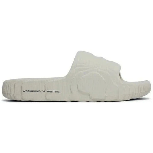 Hier ist der passende **Alt-Text** für das Bild:

**Alt-Text:**
Adidas Adilette 22 Slides in Aluminium-Grau, seitliche Ansicht der Sandale mit dem Schriftzug „The Brand with the Three Stripes“ auf weißem Hintergrund, minimalistisches Design mit strukturiertem Muster.