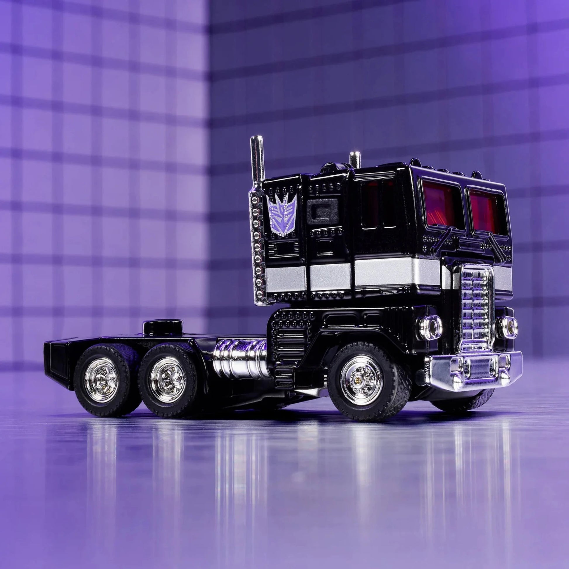 Hot Wheels Nemesis Prime Truck – schwarzer Premium-Sammlertruck mit silbernen Details und roter Scheibenoptik, präsentiert auf lila Hintergrund im futuristischen Stil.